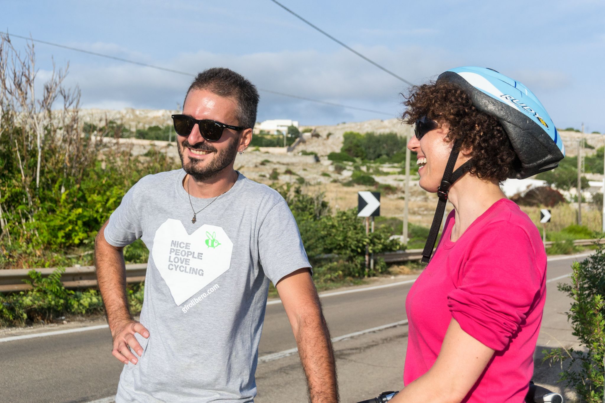 Coppia di ciclisti, occhiali da sole, paesaggio brullo, strada, vacanza all'aria aperta in bici, in Puglia tra Matera e Lecce